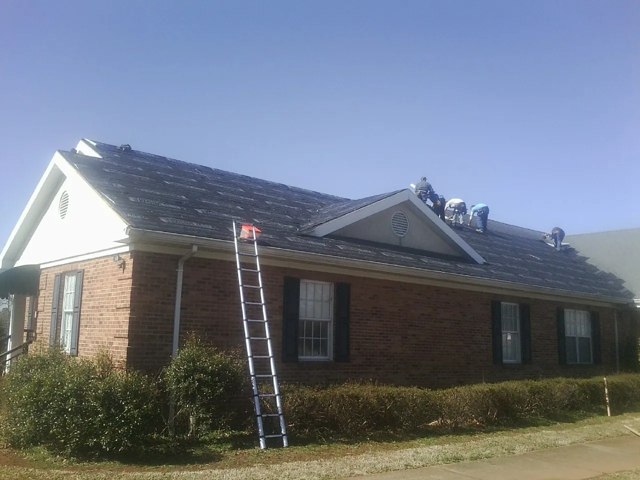 Crew tearing shingles off a brick ranch roof with a ladder set — Metal Roof Repair work by our crew in Pasadena