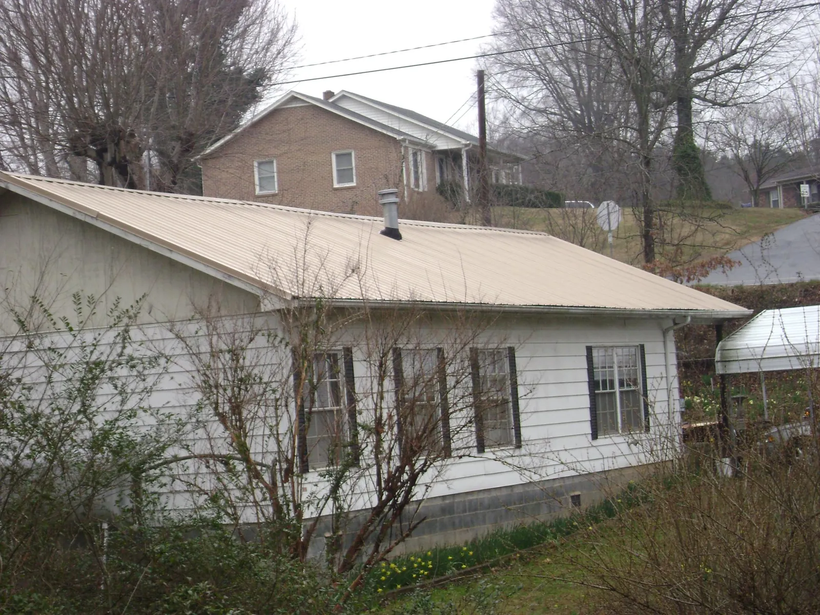 Tan metal roof on a white sided house set into a hillside — Commercial Roofing by Roofing Brothers in Pasadena